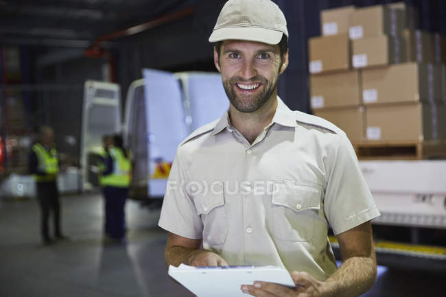 Ritratto sorridente camionista con appunti alla banchina di carico del magazzino di distribuzione — Foto stock