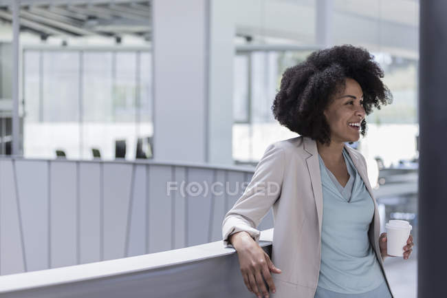 Smiling businesswoman drinking coffee at office railing — Stock Photo