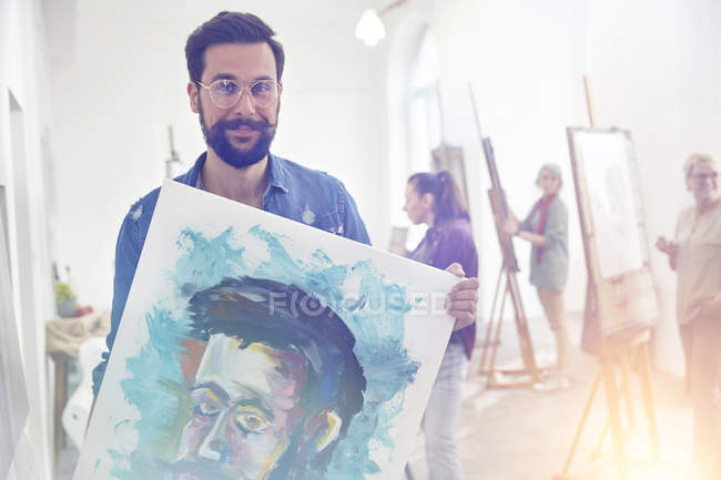 Porträt lächelnder, selbstbewusster, stolzer männlicher Künstler mit Malerei im Atelier des Kunstkurses — Stockfoto