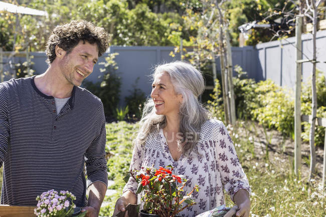 Happy couple carrying potted flowers, gardening in sunny garden — Stock Photo