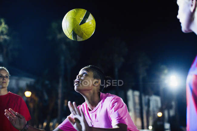 Giovane giocatore di calcio femminile testa la palla sul campo di notte — Foto stock