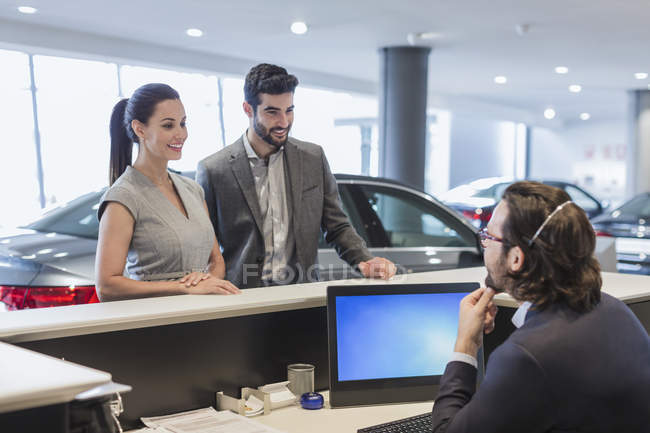Couple de clients parlant à la réceptionniste masculine au bureau dans la salle d'exposition concessionnaire automobile — Photo de stock