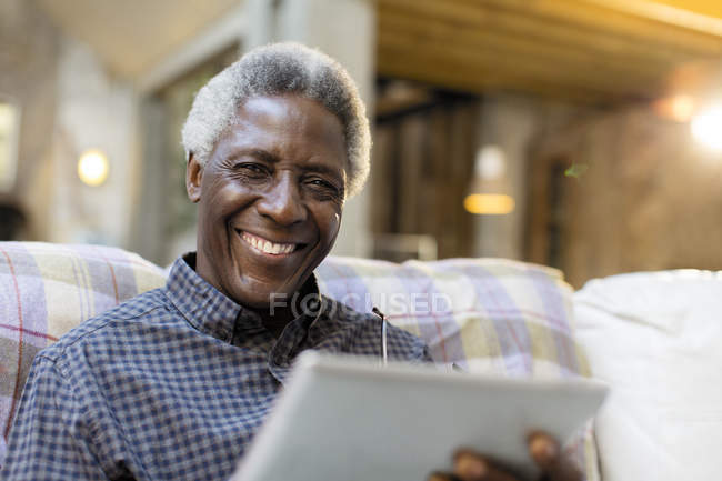 Retrato sonriente, hombre mayor con confianza utilizando tableta digital en el sofá - foto de stock