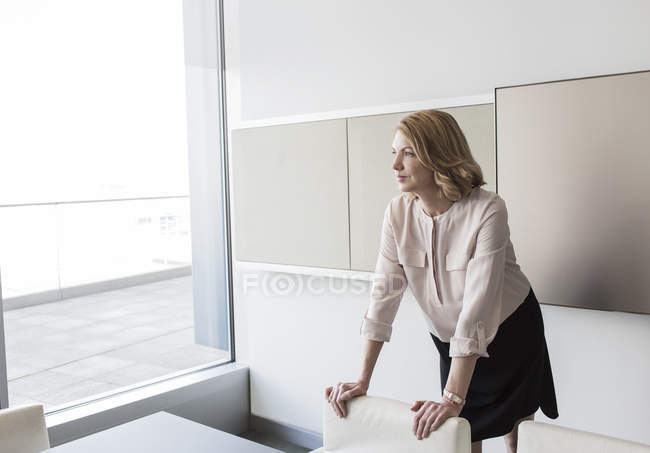 Mujer de negocios pensativa mirando por la ventana de la oficina - foto de stock