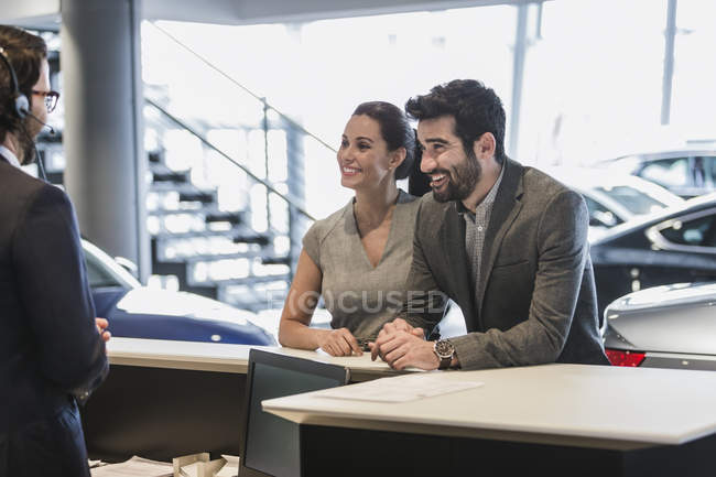 Couple customers talking to receptionist at desk in car dealership showroom — Stock Photo