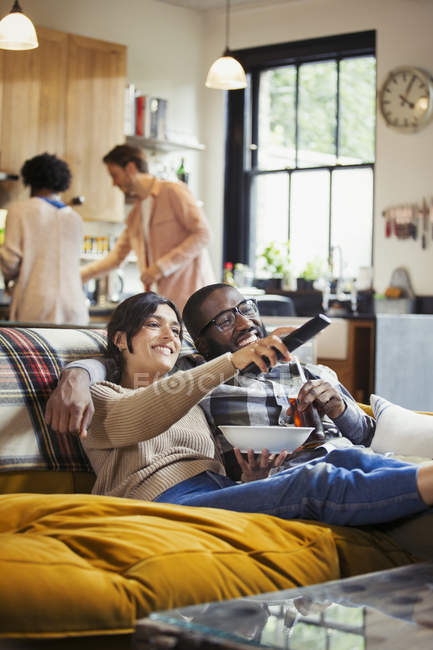 Couple souriant et affectueux regardant la télévision et mangeant du pop-corn sur le canapé du salon — Photo de stock