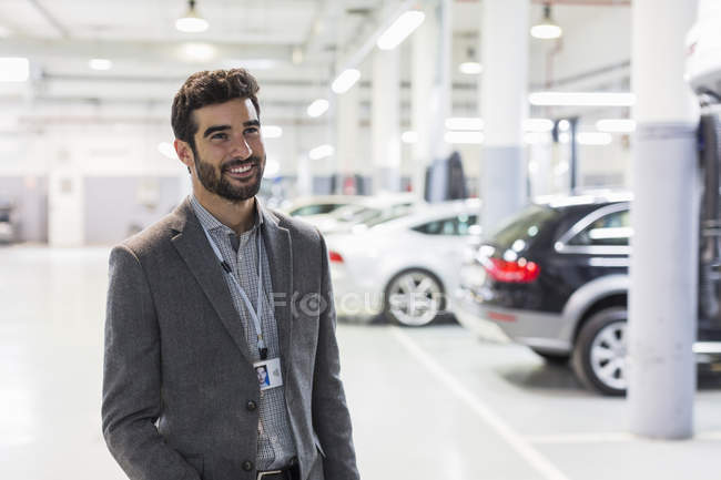 Ritratto sorridente venditore di auto guardando altrove in concessionaria auto officina di riparazione auto — Foto stock