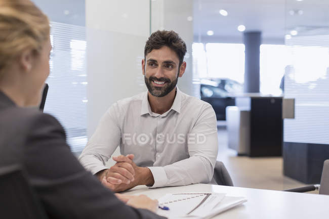 Sourire client masculin à l'écoute de la vendeuse de voiture dans le bureau de concessionnaire automobile — Photo de stock