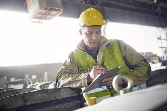 Stahlarbeiter schreibt auf Klemmbrett in Stahlwerk — Stockfoto