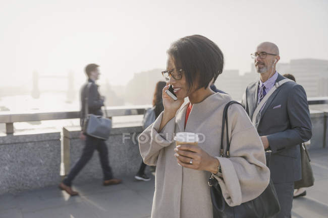 Silhouette businesswoman talking on cell phone and drinking coffee on urban bridge, London, UK — Stock Photo