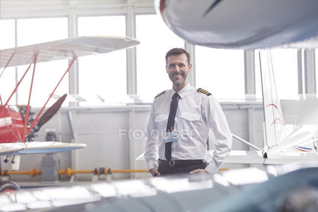 Portrait smiling male pilot standing near airplane in hangar — Stock Photo