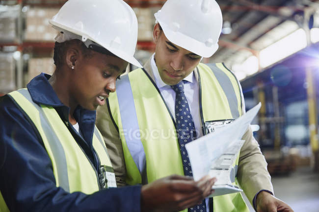 Gerente y trabajador revisando papeleo en almacén de distribución - foto de stock