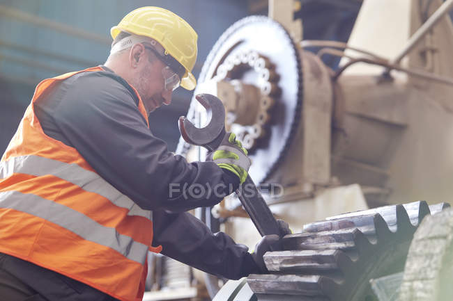 Trabajador masculino usando llave inglesa grande en el engranaje en fábrica - foto de stock
