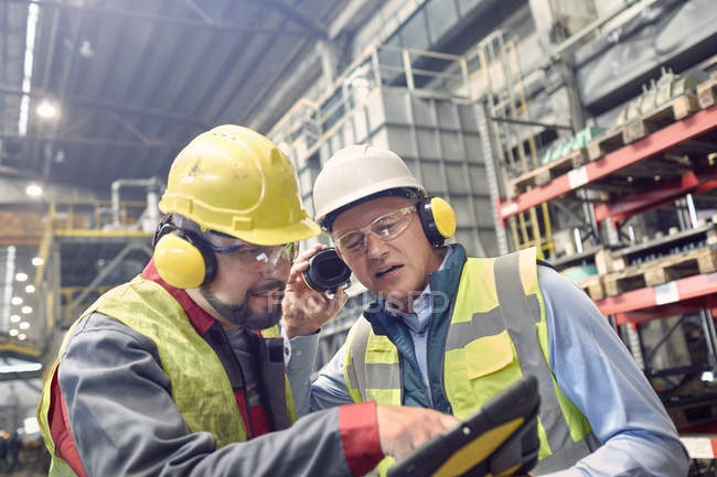 Trabajadores siderúrgicos que usan protectores de oídos usando tableta digital en molino de acero - foto de stock