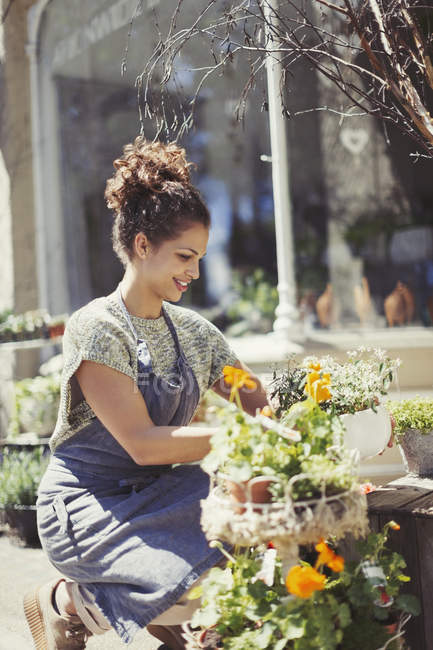 Floristería femenina arreglando exhibición en tienda de flores soleada tienda - foto de stock
