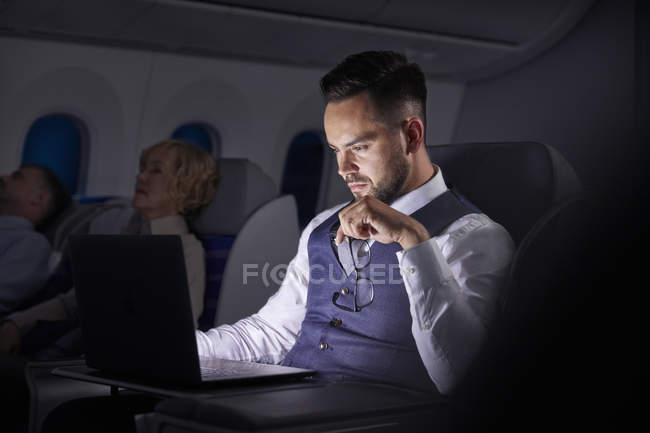Uomo d'affari serio che lavora al computer portatile in aereo durante la notte — Foto stock