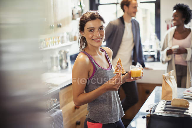 Портрет усміхненої молодої жінки, що їсть тост і п'є апельсиновий сік на кухні — стокове фото