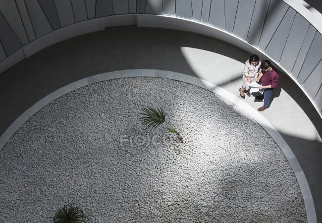 Empresario y mujer de negocios discutiendo papeleo en un patio soleado y moderno - foto de stock