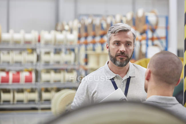 Supervisor masculino serio escuchando al trabajador en la fábrica de fibra óptica - foto de stock