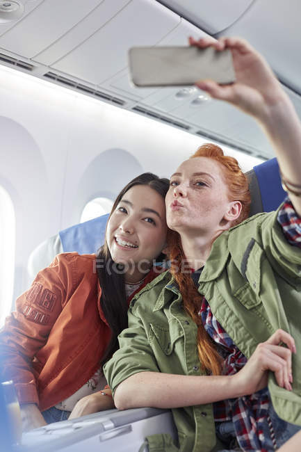 Young women friends with camera phone posing for selfie on airplane — Stock Photo