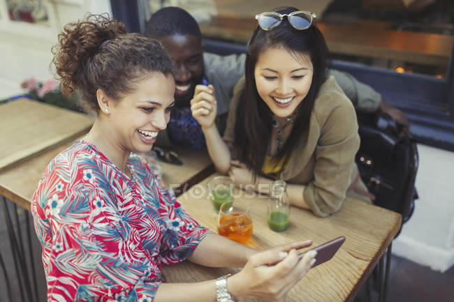 Jóvenes amigas usando teléfono inteligente en la cafetería de la acera - foto de stock
