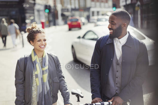Casal sorridente viajando com bicicleta na ensolarada rua urbana — Fotografia de Stock