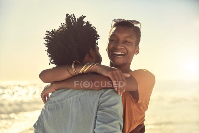 Rindo jovem casal abraçando na praia ensolarada de verão — Fotografia de Stock