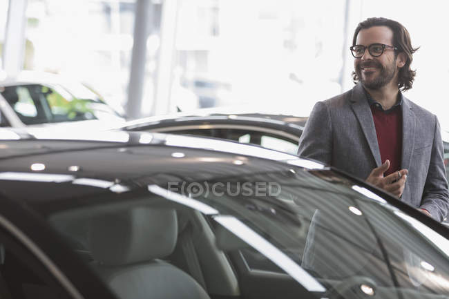 Uomo sorridente sfogliando nuove auto in concessionaria auto showroom — Foto stock