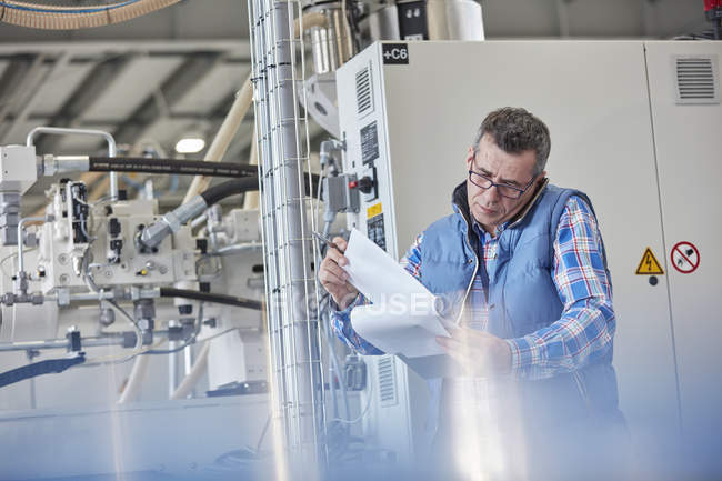 Male supervisor with clipboard talking on cell phone in factory — Stock Photo