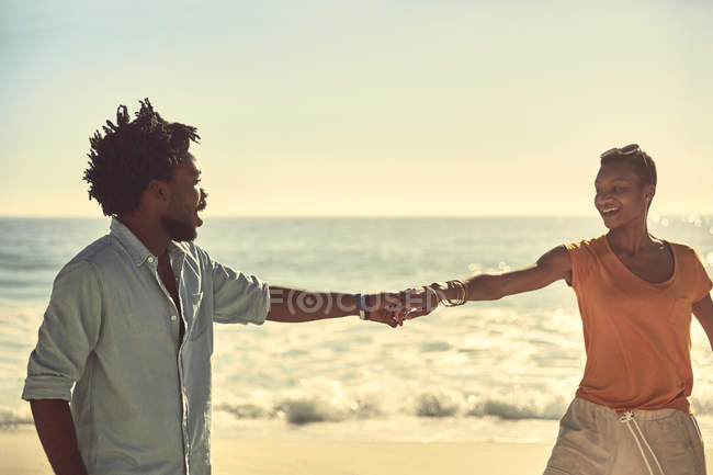Прихильна молода пара тримає руки на сонячному літньому пляжі — стокове фото