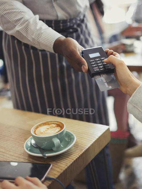 Cliente pagando camarero con lector de tarjetas de crédito en la mesa de café - foto de stock
