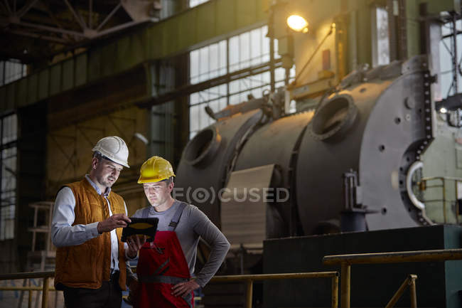 Male engineer and worker using digital tablet in dark factory — Stock Photo