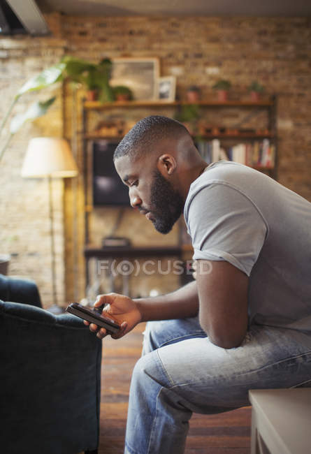 Giovane uomo sms con smart phone in salotto — Foto stock