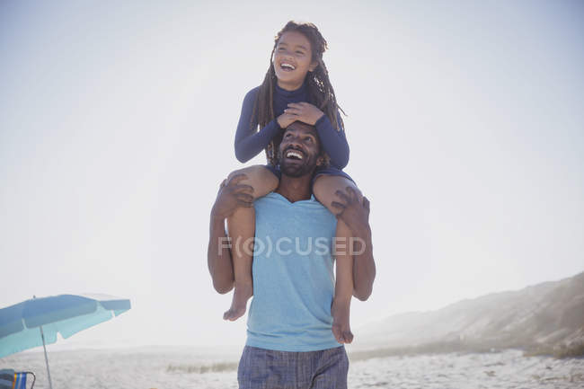 Padre giocoso che porta la figlia sulle spalle sulla soleggiata spiaggia estiva — Foto stock