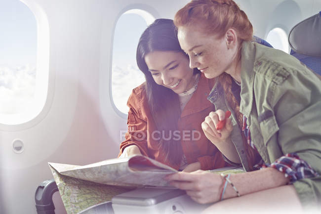 Young women friends looking at map on airplane — Stock Photo