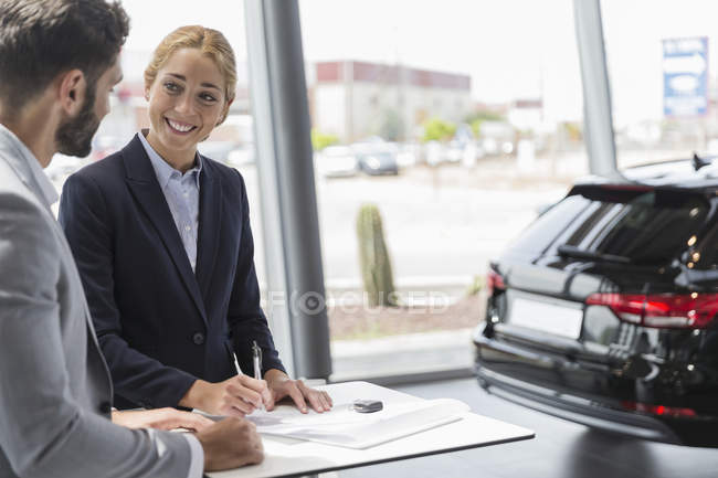 Car saleswoman and male customer signing contract paperwork in car dealership showroom — Stock Photo