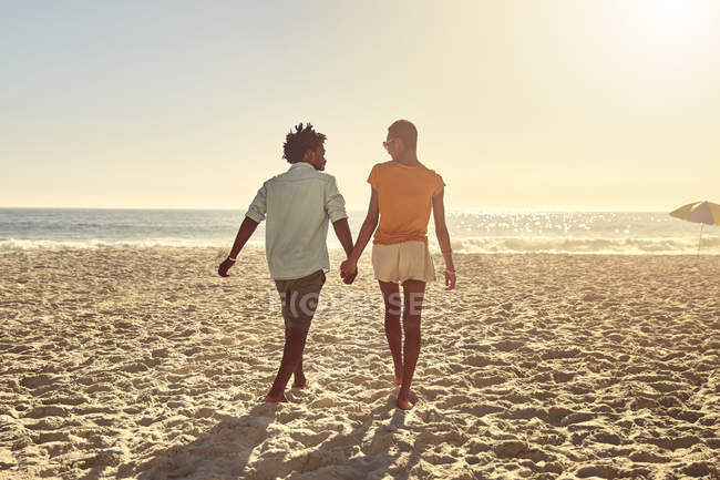 Young couple holding hands, walking on sunny summer beach — Stock Photo
