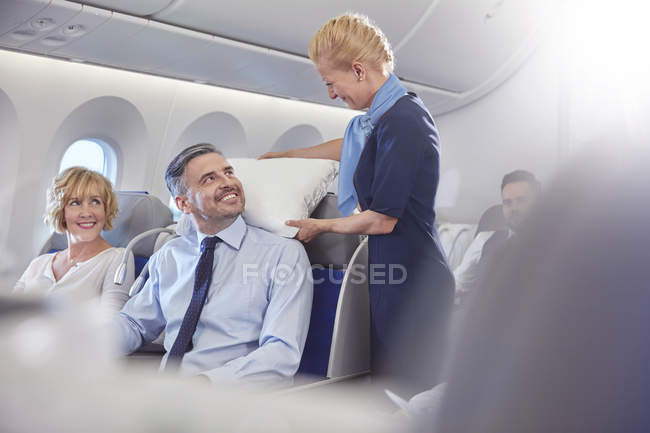 Assistente de bordo sorridente ajustando travesseiro para homem de negócios em primeira classe no avião — Fotografia de Stock