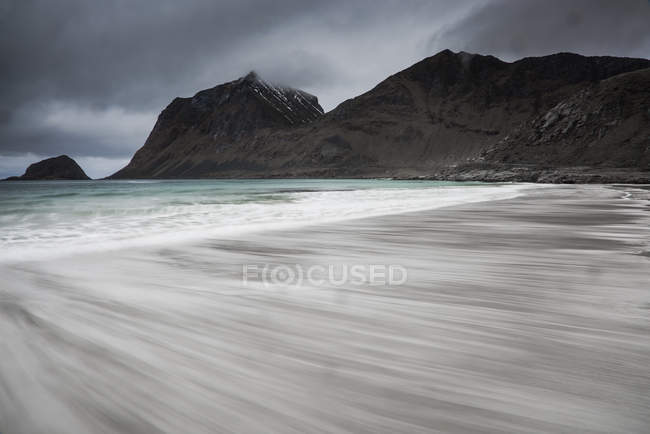 Sfocato moto oceano marea spiaggia sotto montagne frastagliate, Haukland Beach, Lofoten, Norvegia — Foto stock