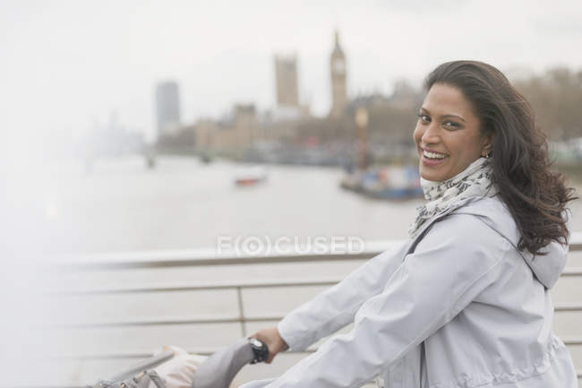 Portrait smiling woman bike riding on bridge over Thames River, London, UK — Stock Photo