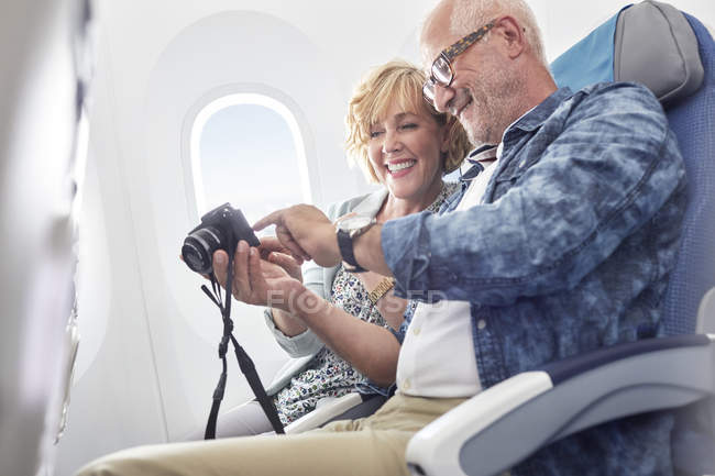 Mature couple looking at photos on digital camera on airplane — Stock Photo