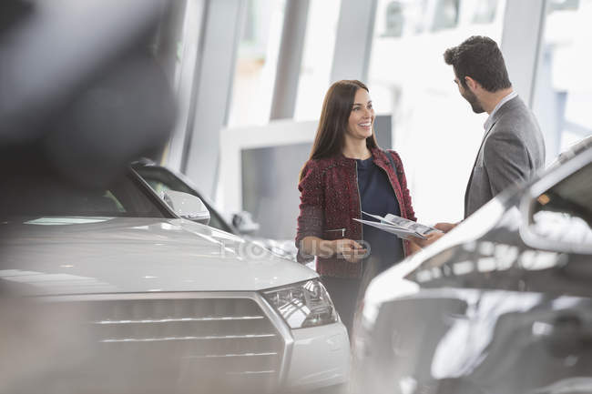 Car saleswoman showing brochure to male customer in car dealership showroom — Stock Photo