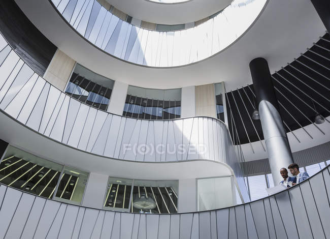Empresarios discutiendo papeleo en arquitectura, balcón moderno atrio de la oficina - foto de stock