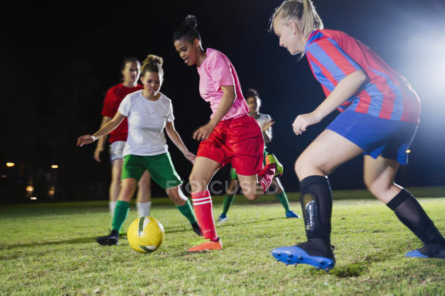 Jovens jogadoras de futebol jogando em campo à noite, correndo para a bola — Fotografia de Stock