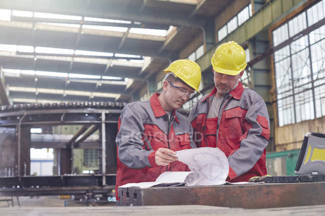 Чоловіки-інженери, які оглядають креслення на заводі — стокове фото