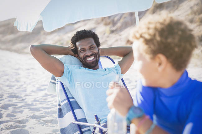 Батько посміхається синові на сонячному літньому пляжі — стокове фото