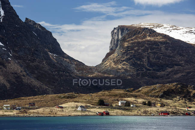 Montañas sobre remotas casas costeras, Krystad, Lofoten, Noruega - foto de stock