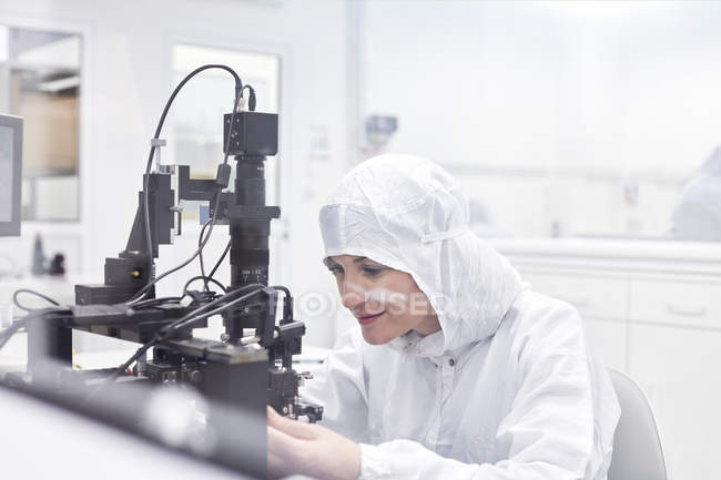 Female engineer in clean suit using equipment in fiber optics research and testing laboratory — Stock Photo