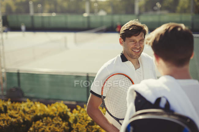 Giovani tennisti maschi che parlano sopra campi da tennis soleggiati — Foto stock