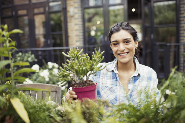 Портрет улыбающейся молодой женщины садоводства с горшочками растений на патио — стоковое фото